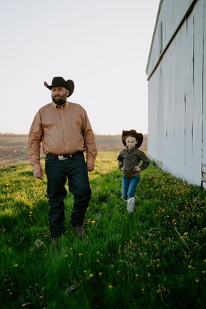 Two figures in cowboy hats walk through tall grass and yellow flowers.