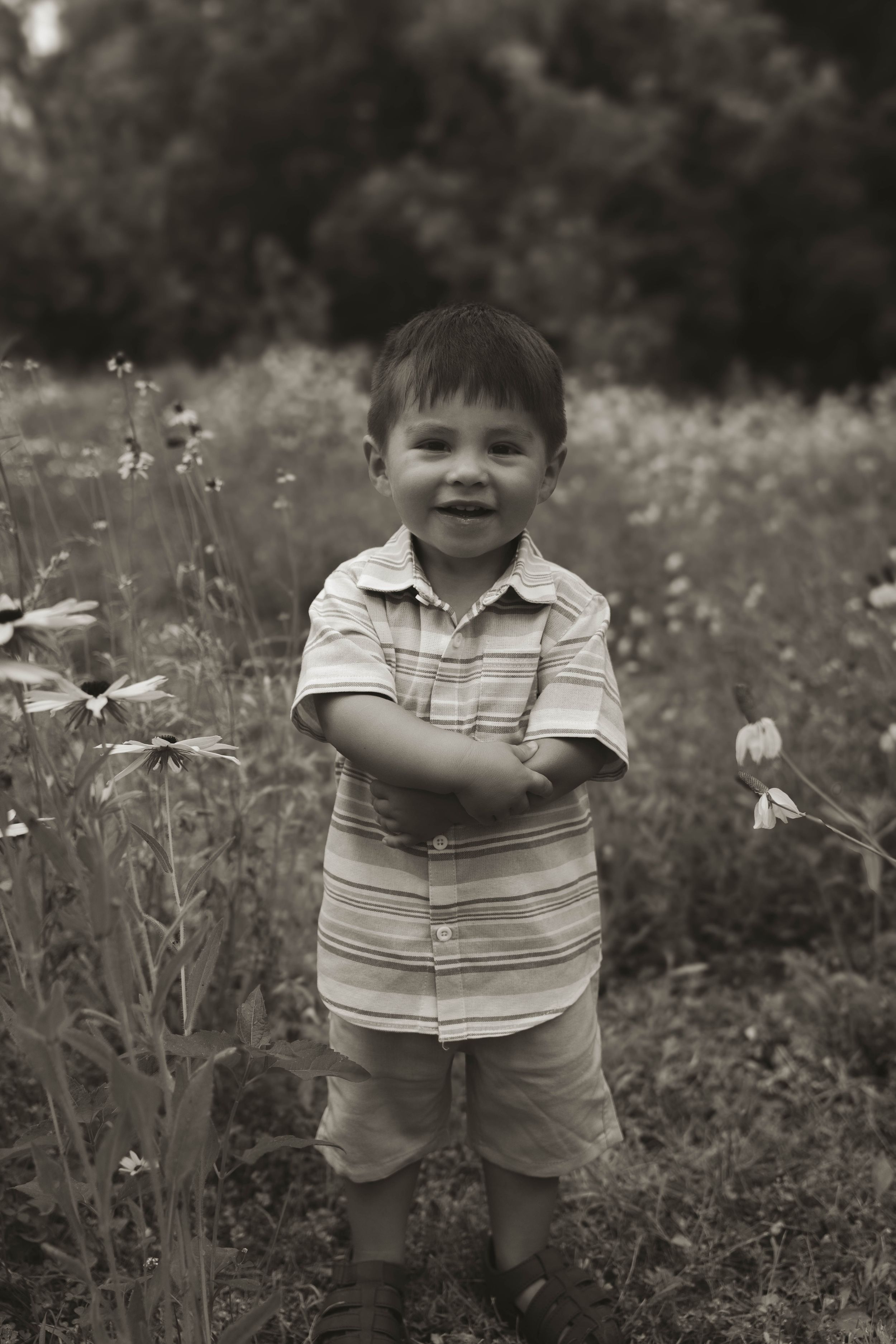 A young child in a striped shirt smiles while standing in a field of wildflowers.