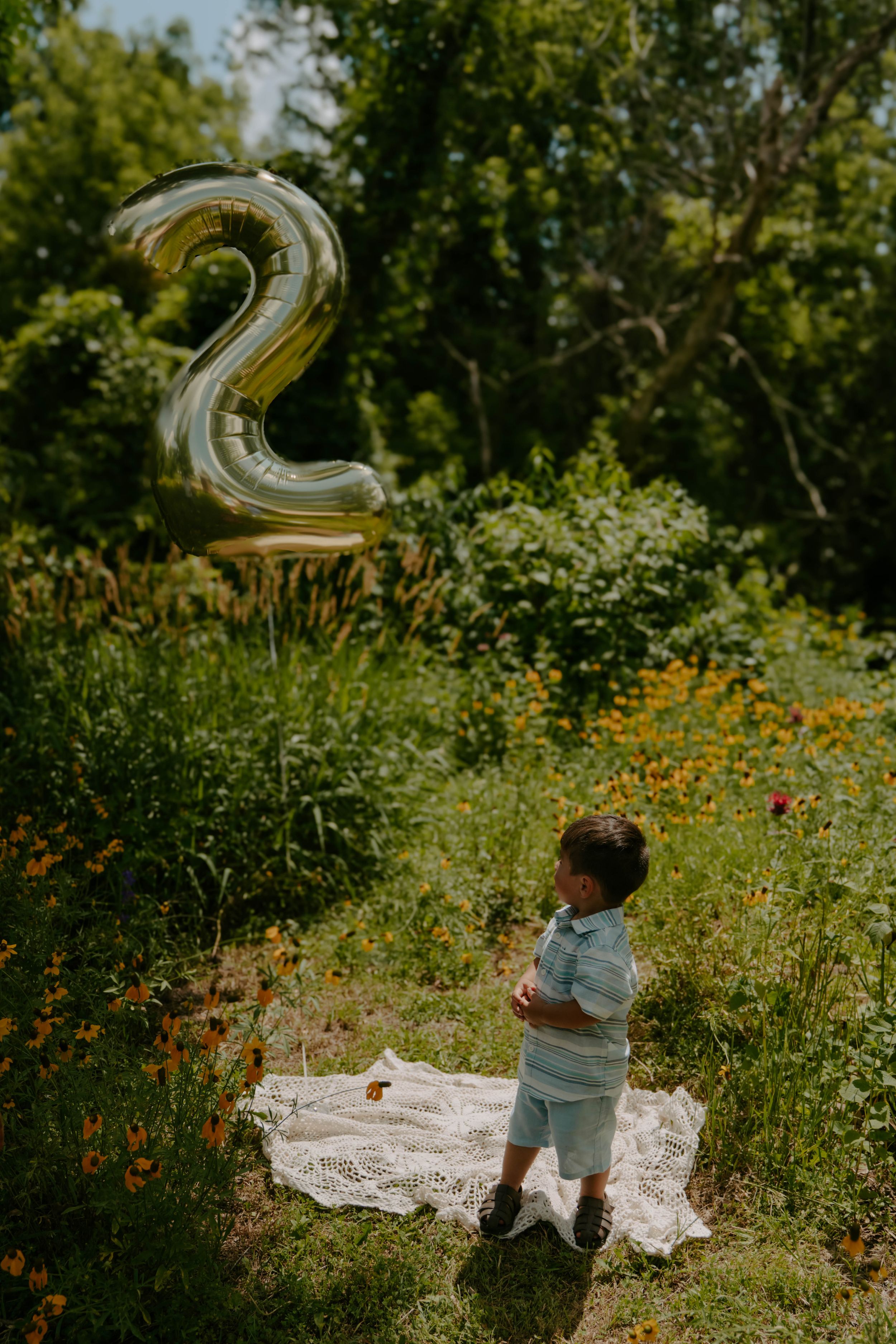 A celebration scene in a wildflower meadow with gold number balloons and a white blanket.