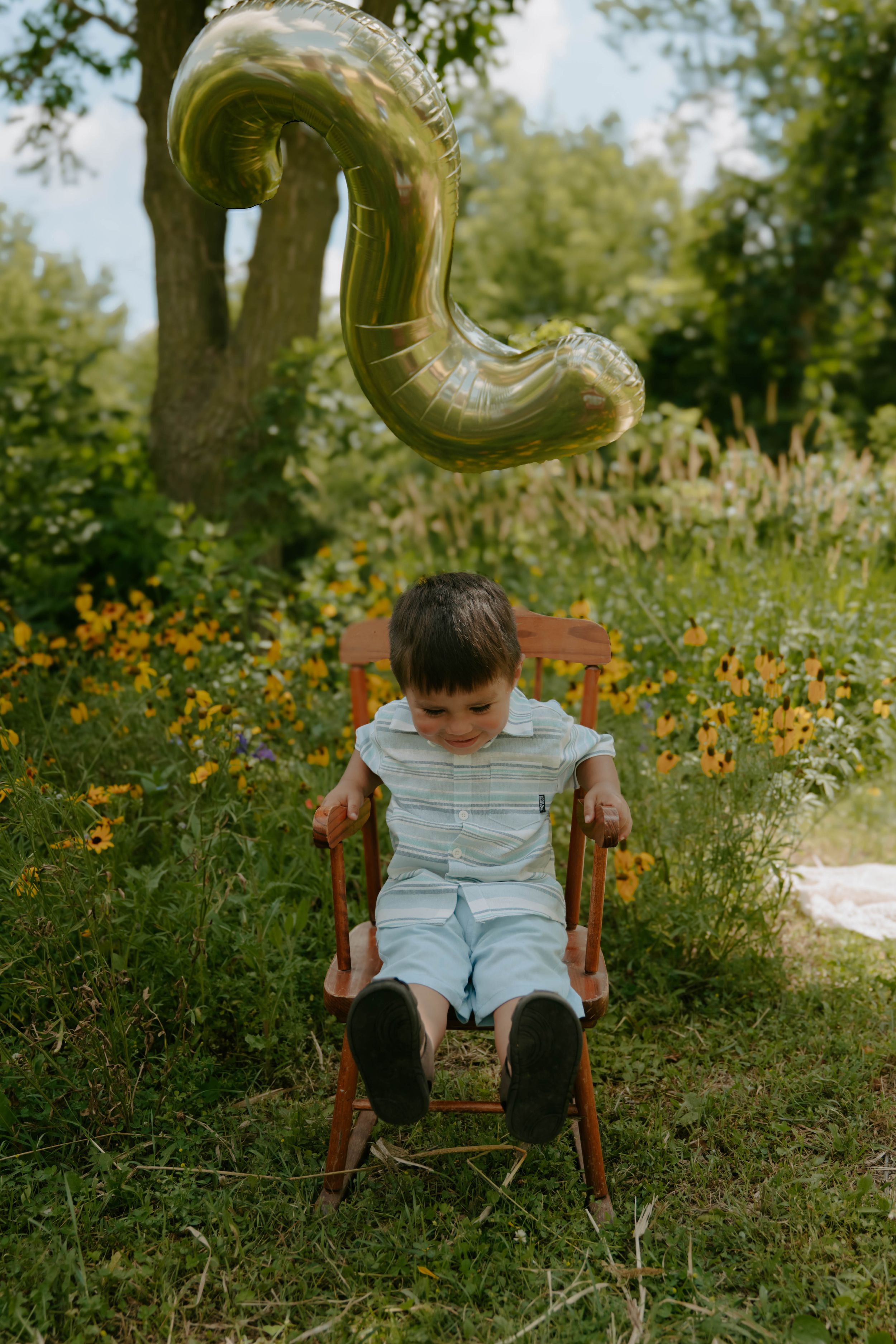 A wooden chair and gold number three balloon decoration in a wildflower garden setting.