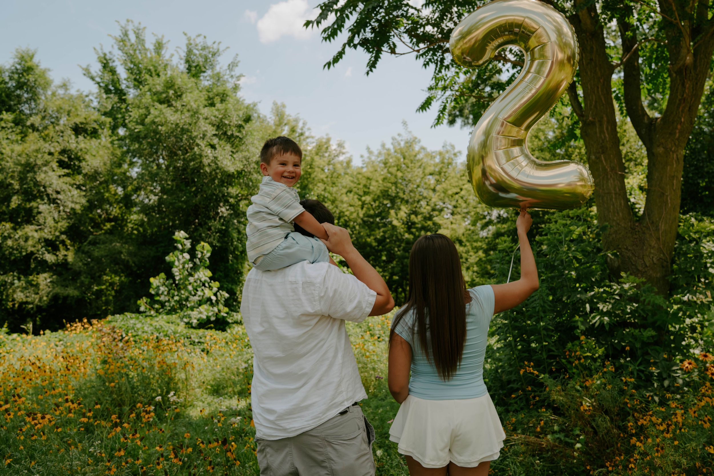 Family members pose with gold number balloons in a natural outdoor setting.