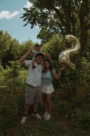 A playful family jumps for joy in a summer garden with metallic balloons.