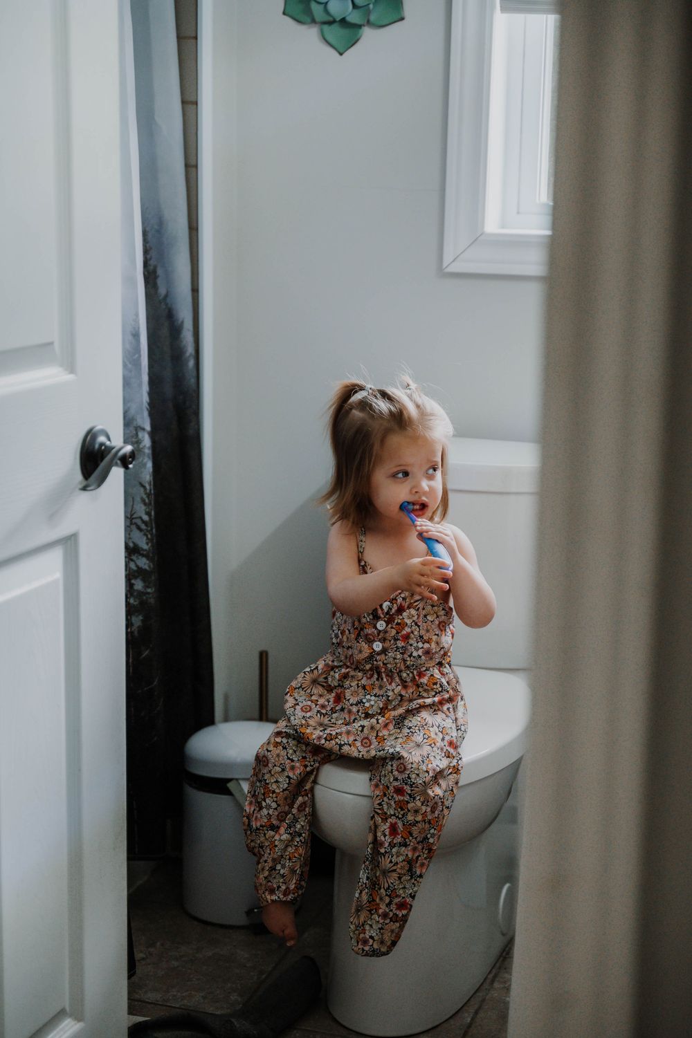 A candid moment captures a toddler sitting on a bathroom toilet with a surprised expression.