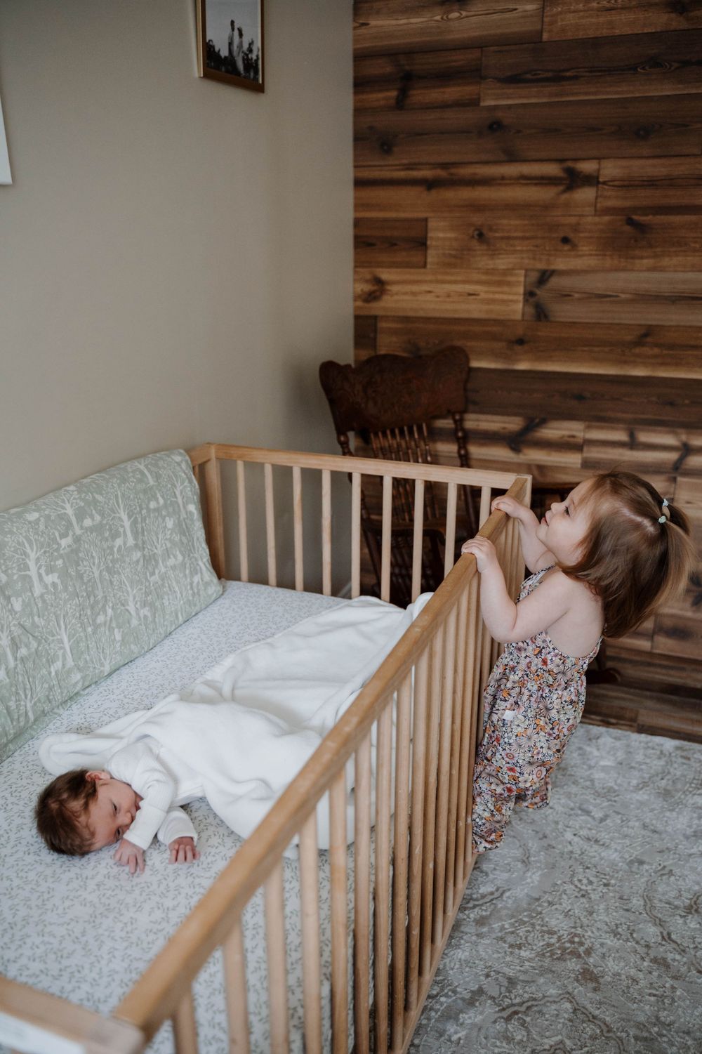 Two children playing and laughing together in a wooden crib with rustic wood panel walls.