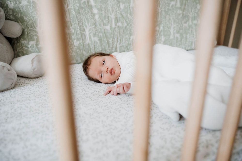 Adorable newborn baby sleeping peacefully on cozy bed while viewed through wooden crib slats in nursery.