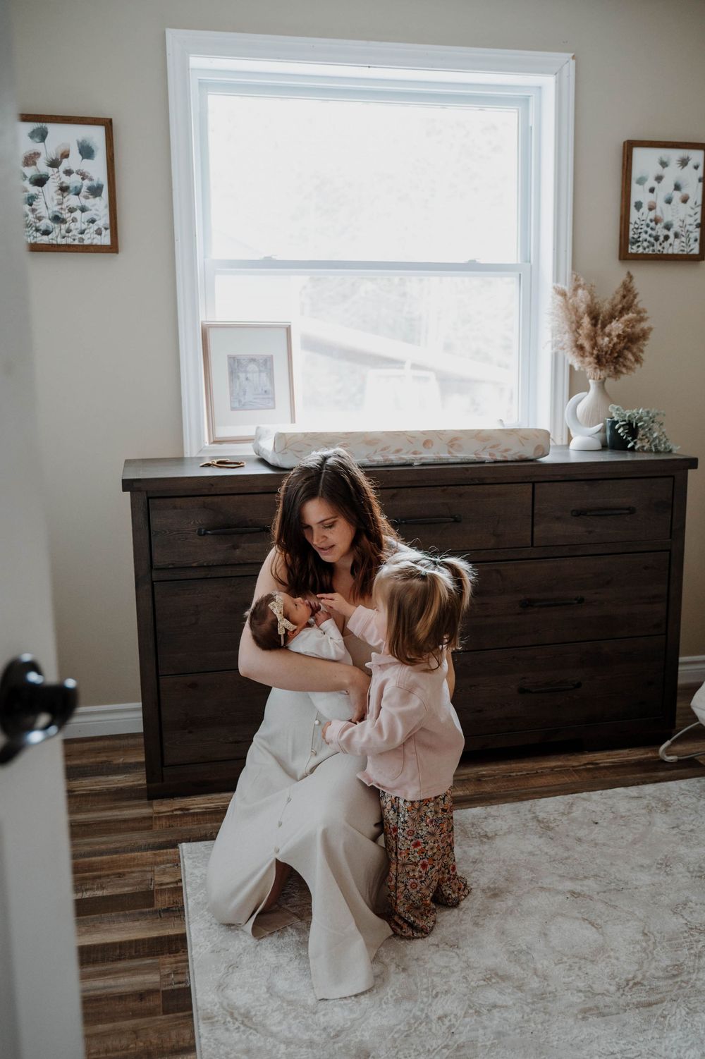 A cozy nursery scene with natural light streaming through a window above a dark wooden dresser.