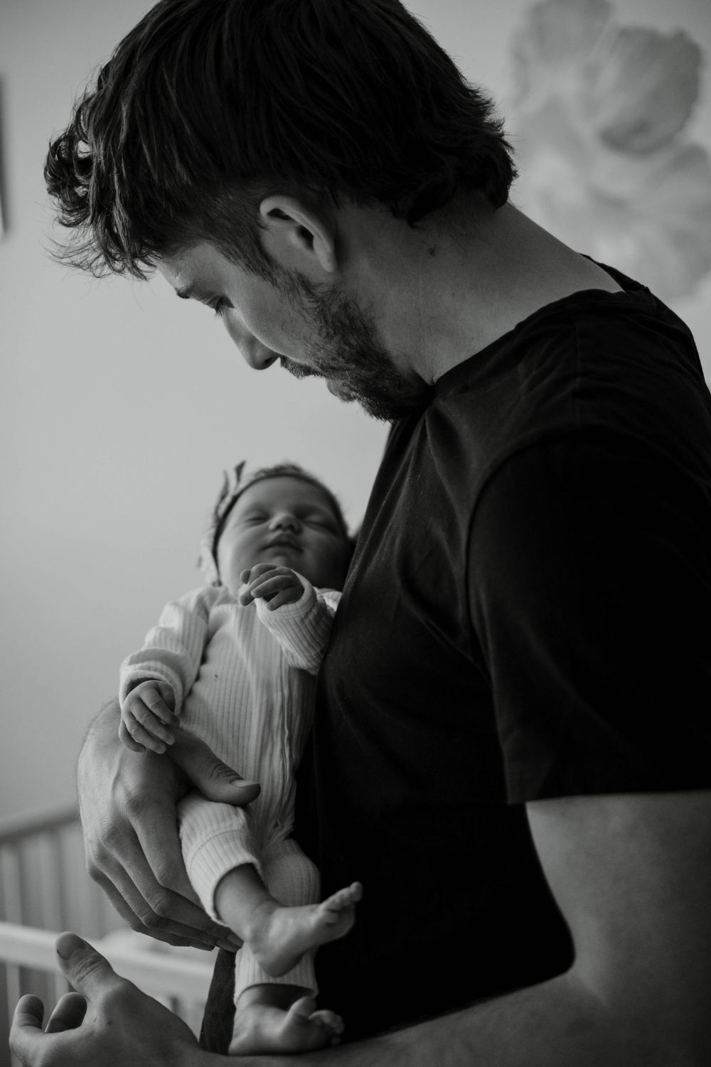 A tender black and white moment showing a newborn being held against a dark background.