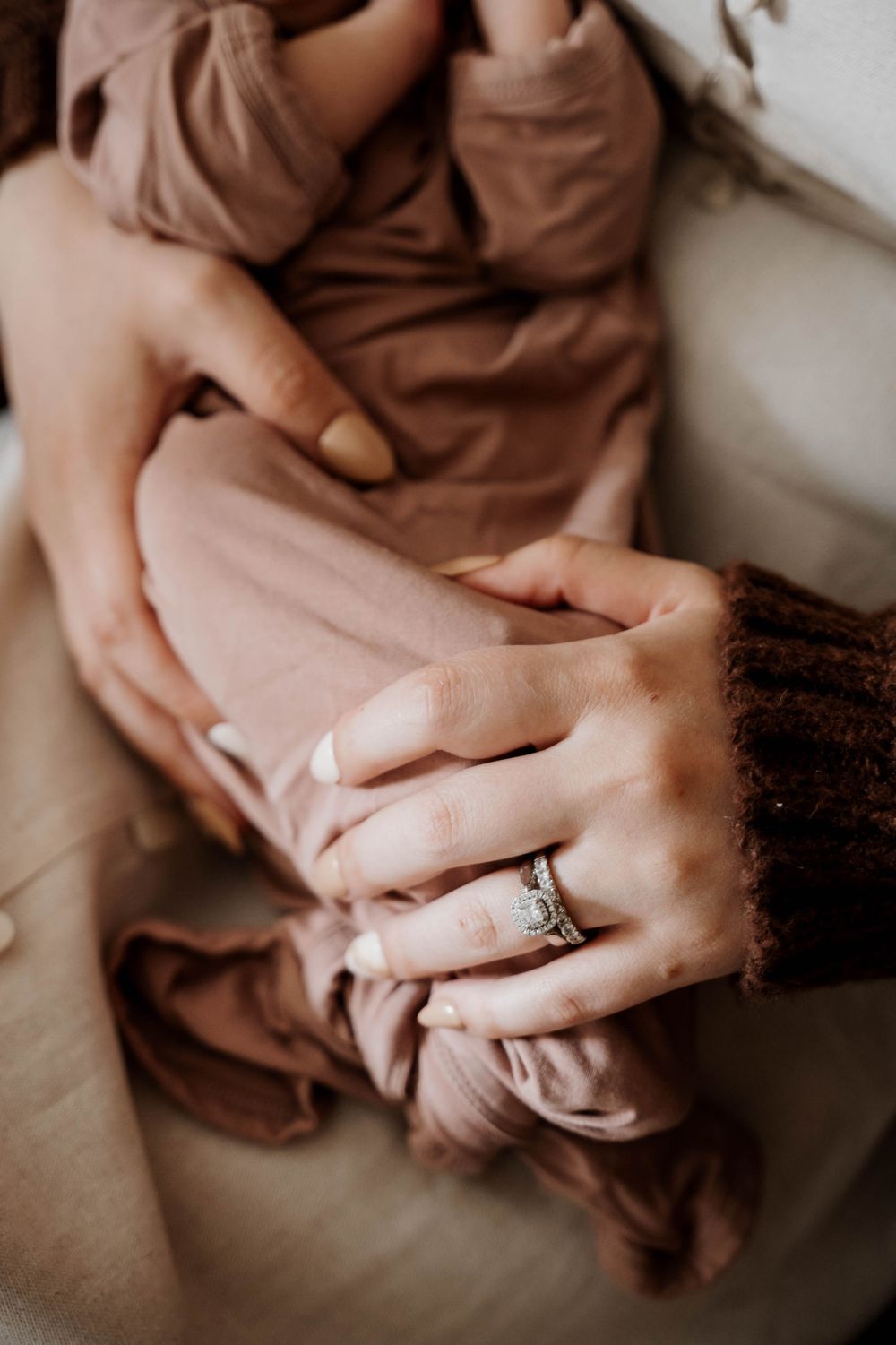 Close-up of hands gently holding fabric with engagement ring visible.