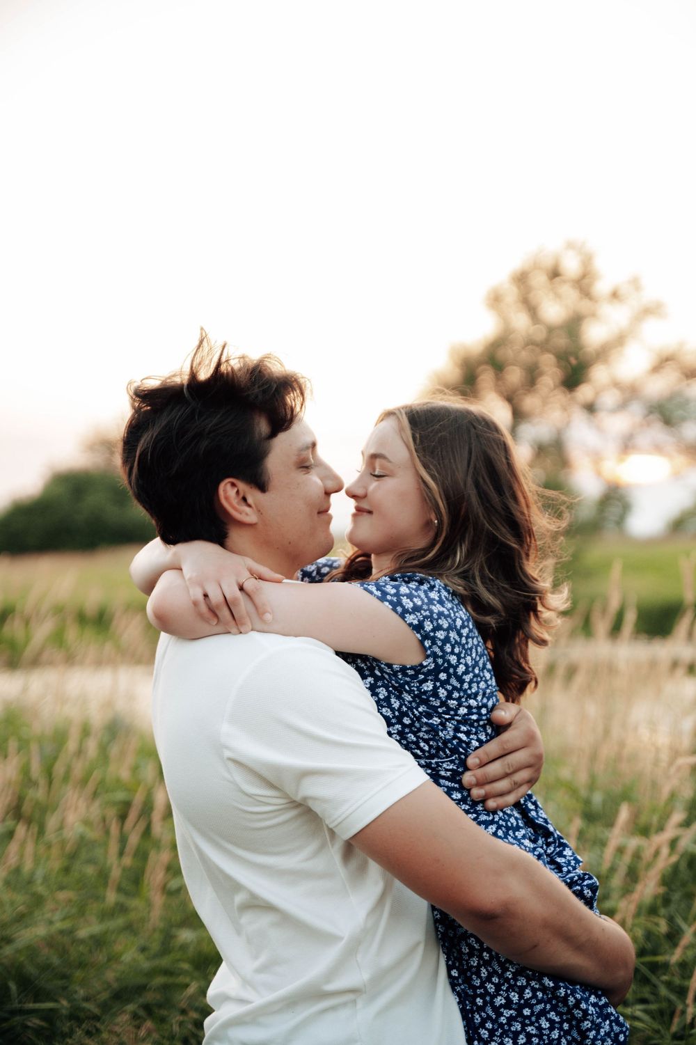 A romantic couple embracing in a golden field during sunset while wearing white and blue polka dot outfits.