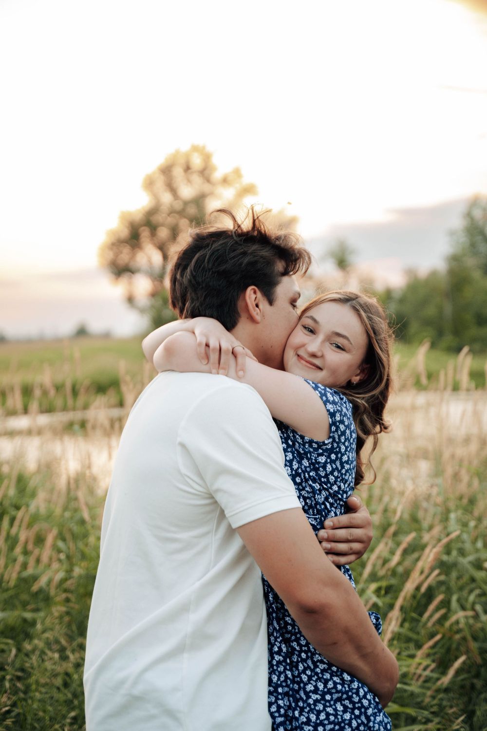 A romantic couple shares tender moments in a field during golden hour photography session.
