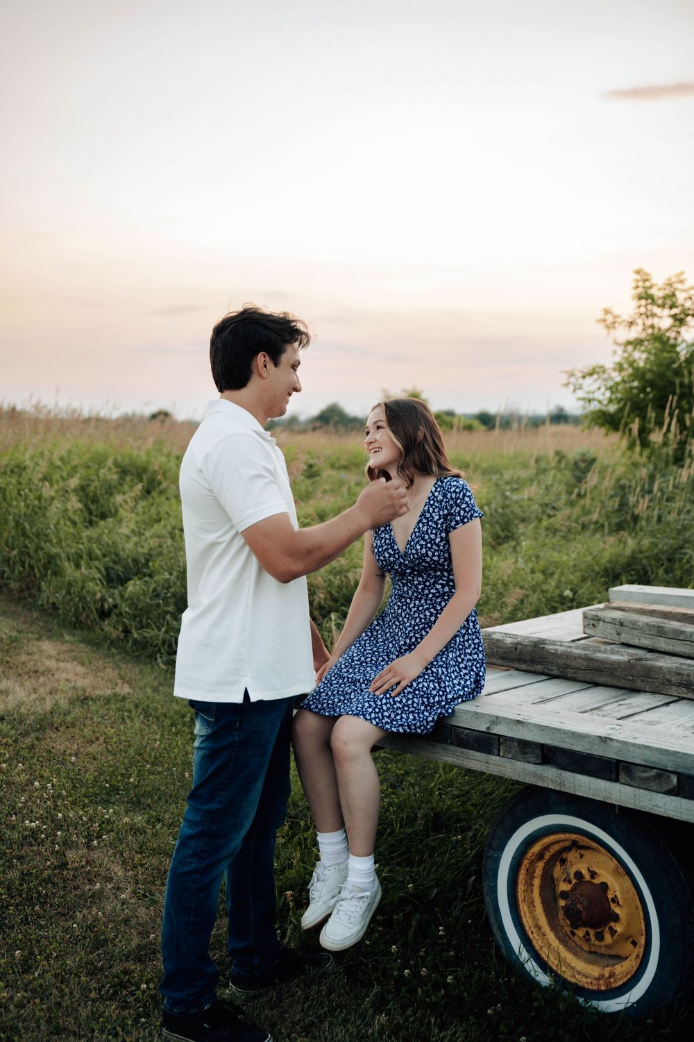 A couple shares an intimate moment sitting on a vintage truck in a rural field at sunset.
