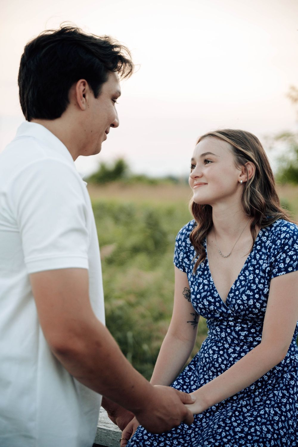 A couple shares an intimate moment outdoors while wearing coordinating blue and white outfits at sunset.