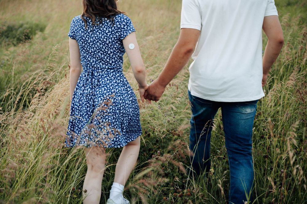 A couple in blue and white outfits walking together through tall grass in a meadow.