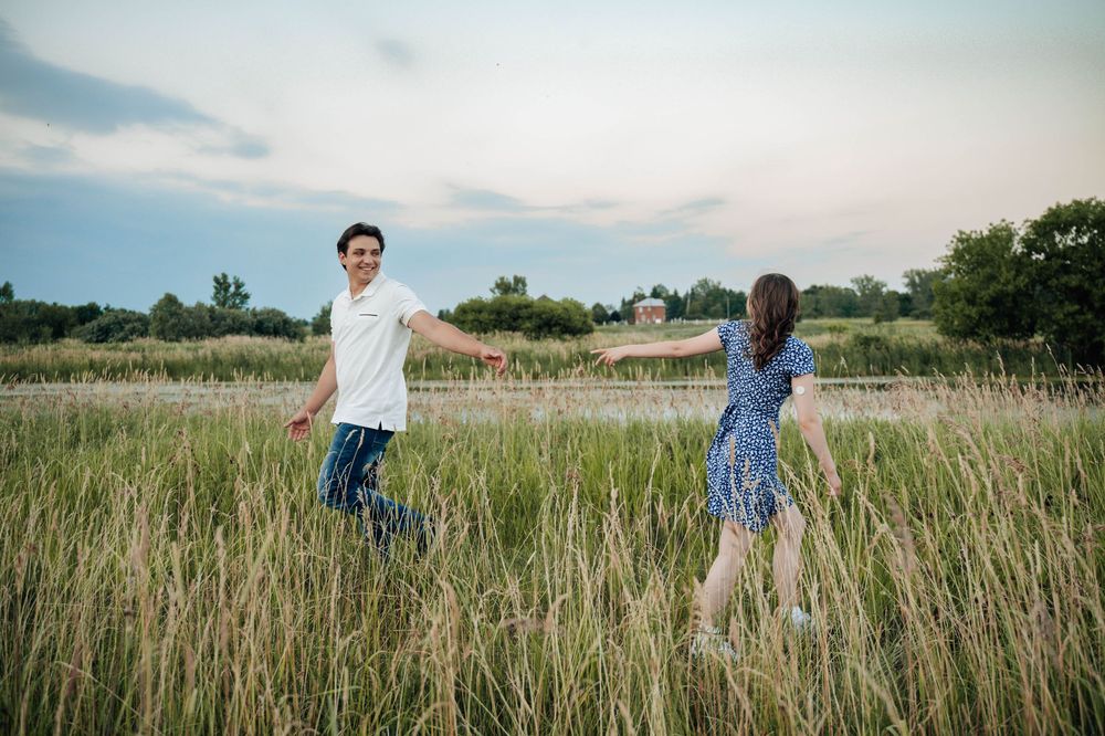 A couple walking through a scenic field of tall grass during a sunset photo shoot.