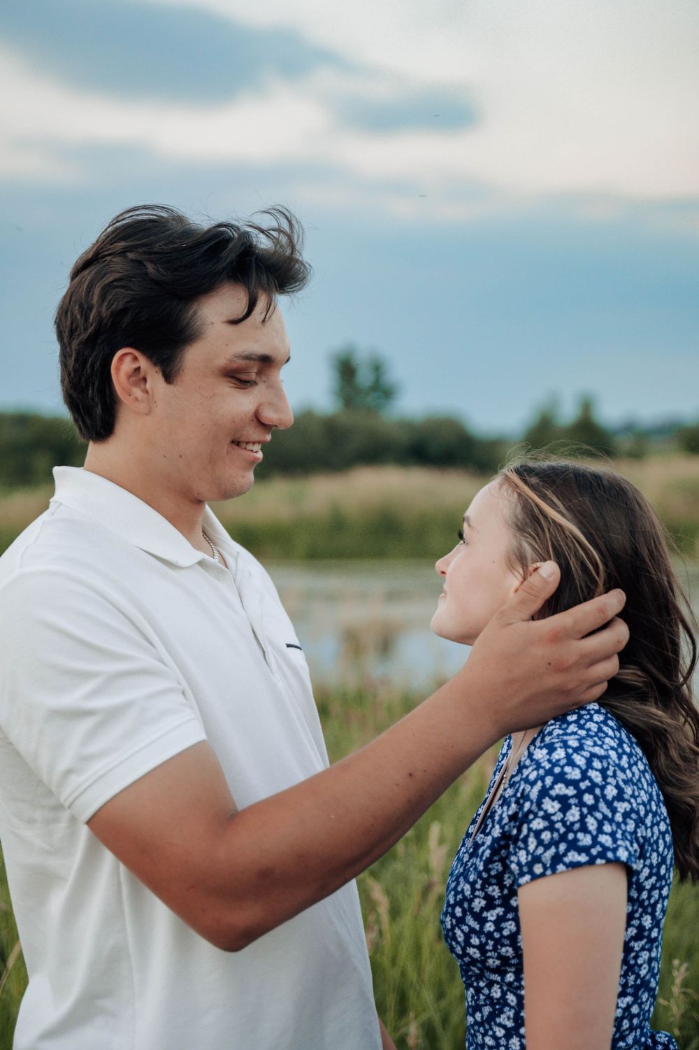Intimate romantic moment shared between a couple in a grassy field under blue skies.