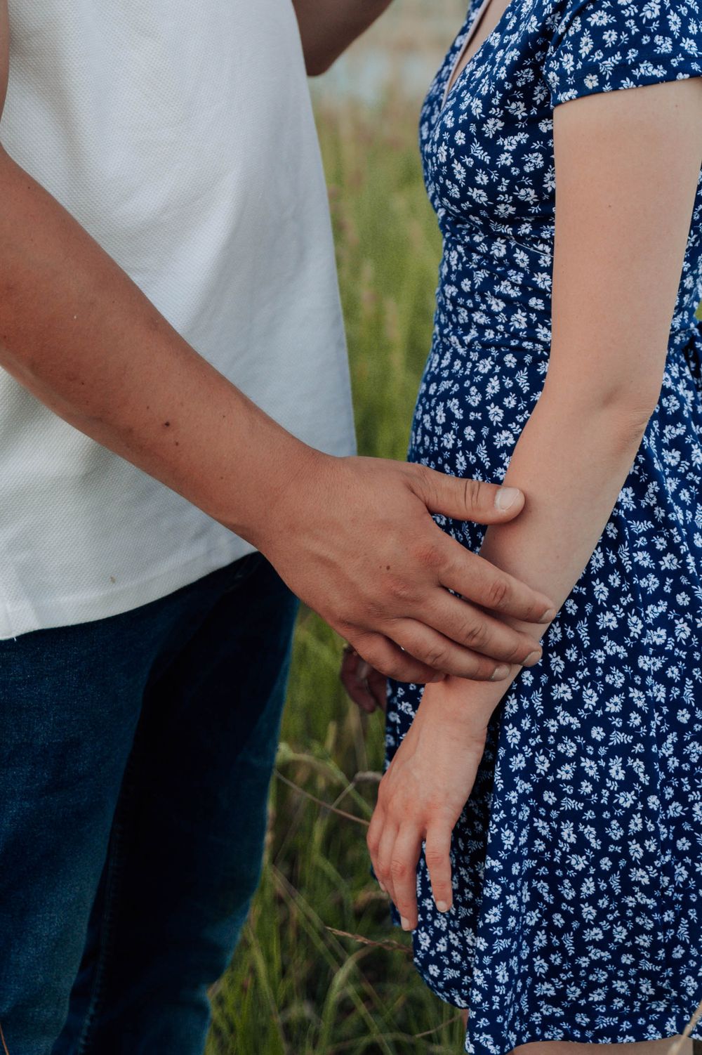 Close-up view of couple's tender embrace in blue floral dress and white shirt outdoors.