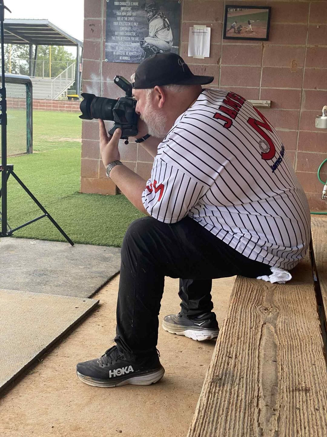 Behind-the-scenes photo shoot setup in a baseball dugout with camera equipment and players in baseball uniforms.
