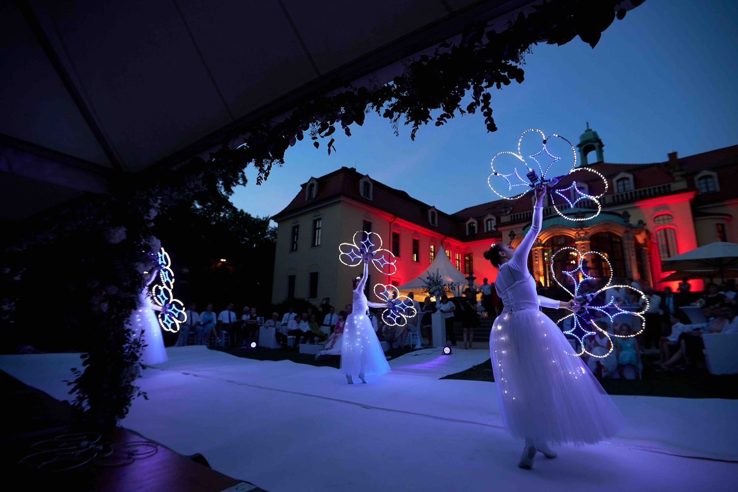 Illuminated outdoor light display in shape of animals and holiday decorations glowing in purple and white.