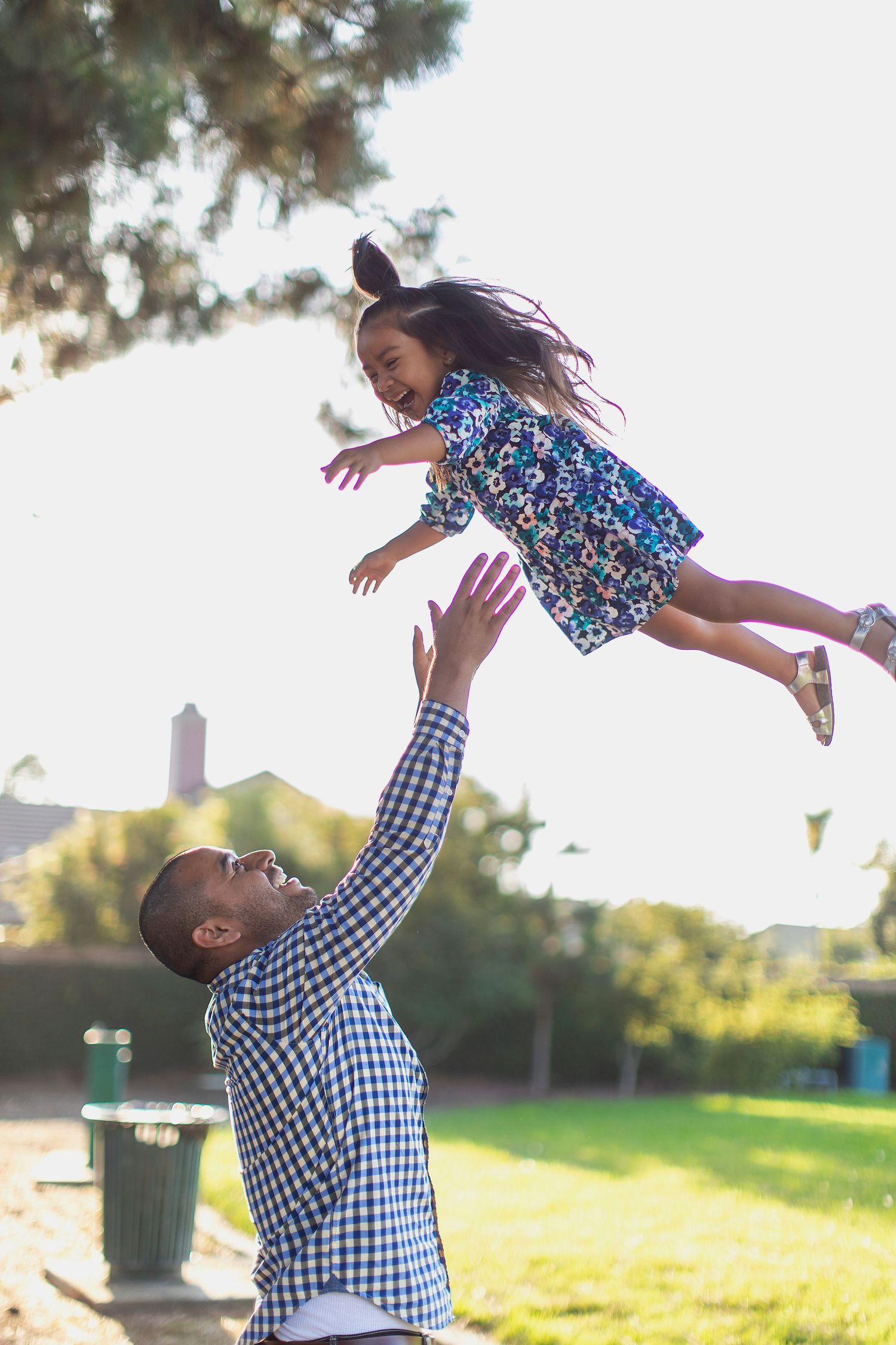 Playful moment captured at a park as a parent lifts a child high in the air.