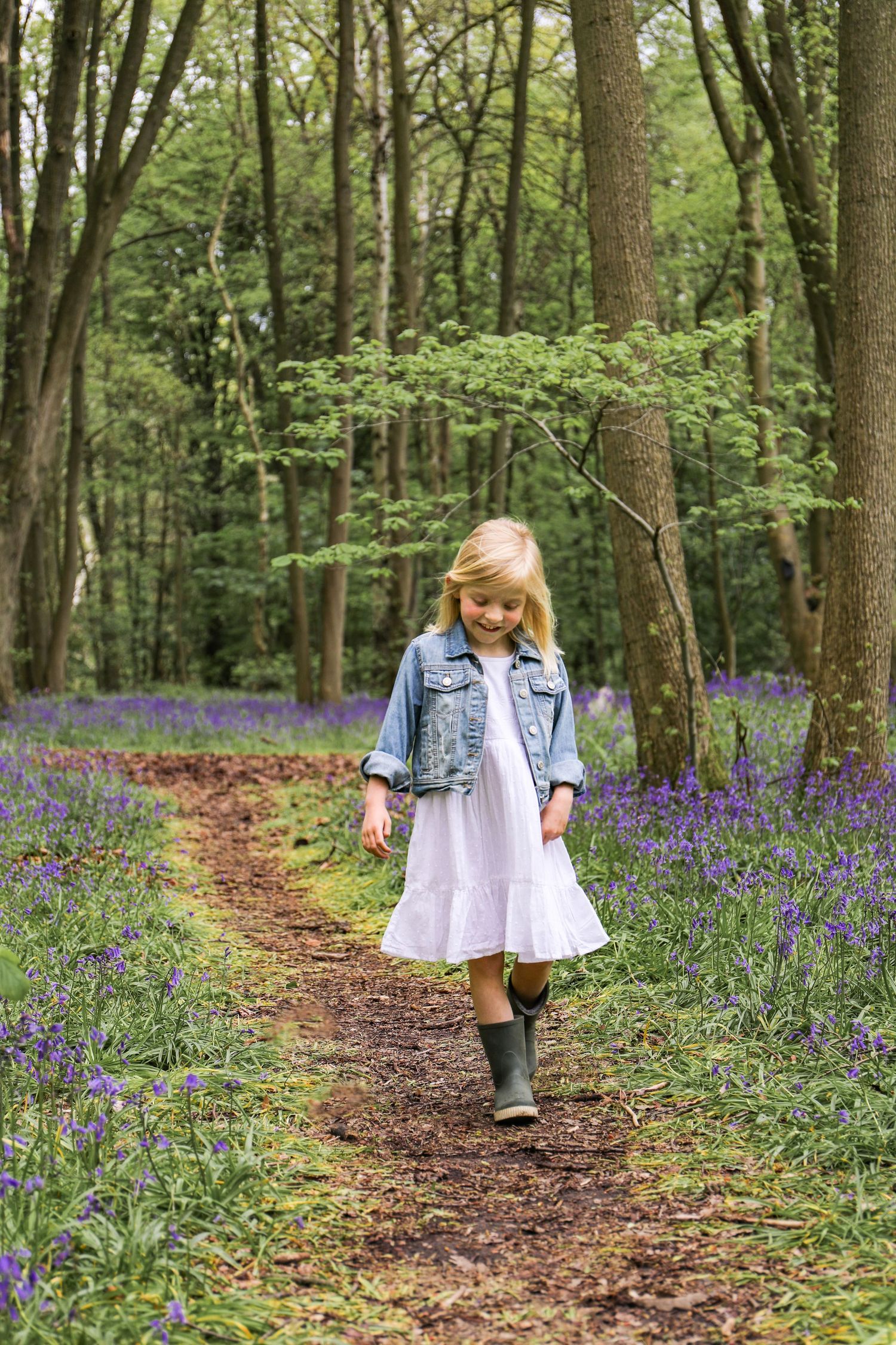 Young girl amongst spring woodland filled with blooming purple bluebells and tall trees, during family shoot in Nottingham