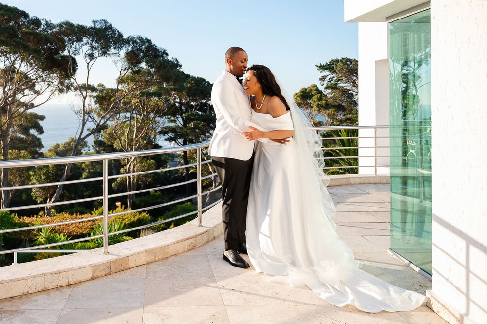 A beautiful romantic moment shared between newlyweds on a white balcony overlooking a scenic coastal view.