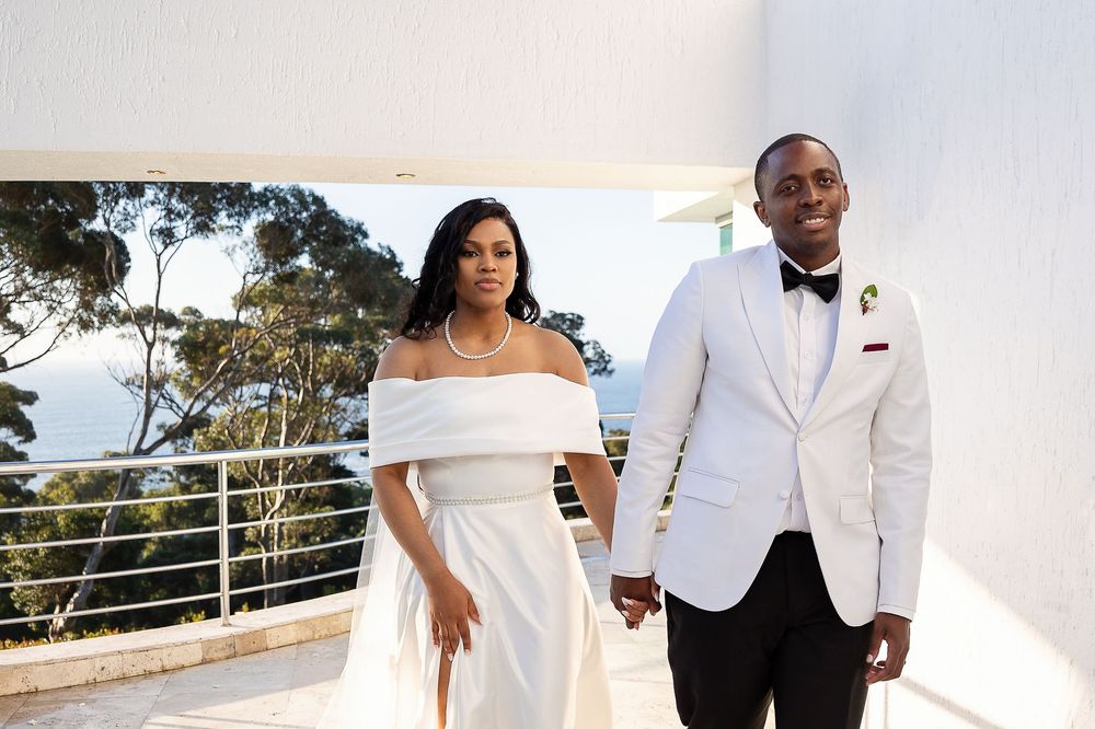 Elegant wedding couple celebrates their special day in crisp white attire against a scenic outdoor backdrop.