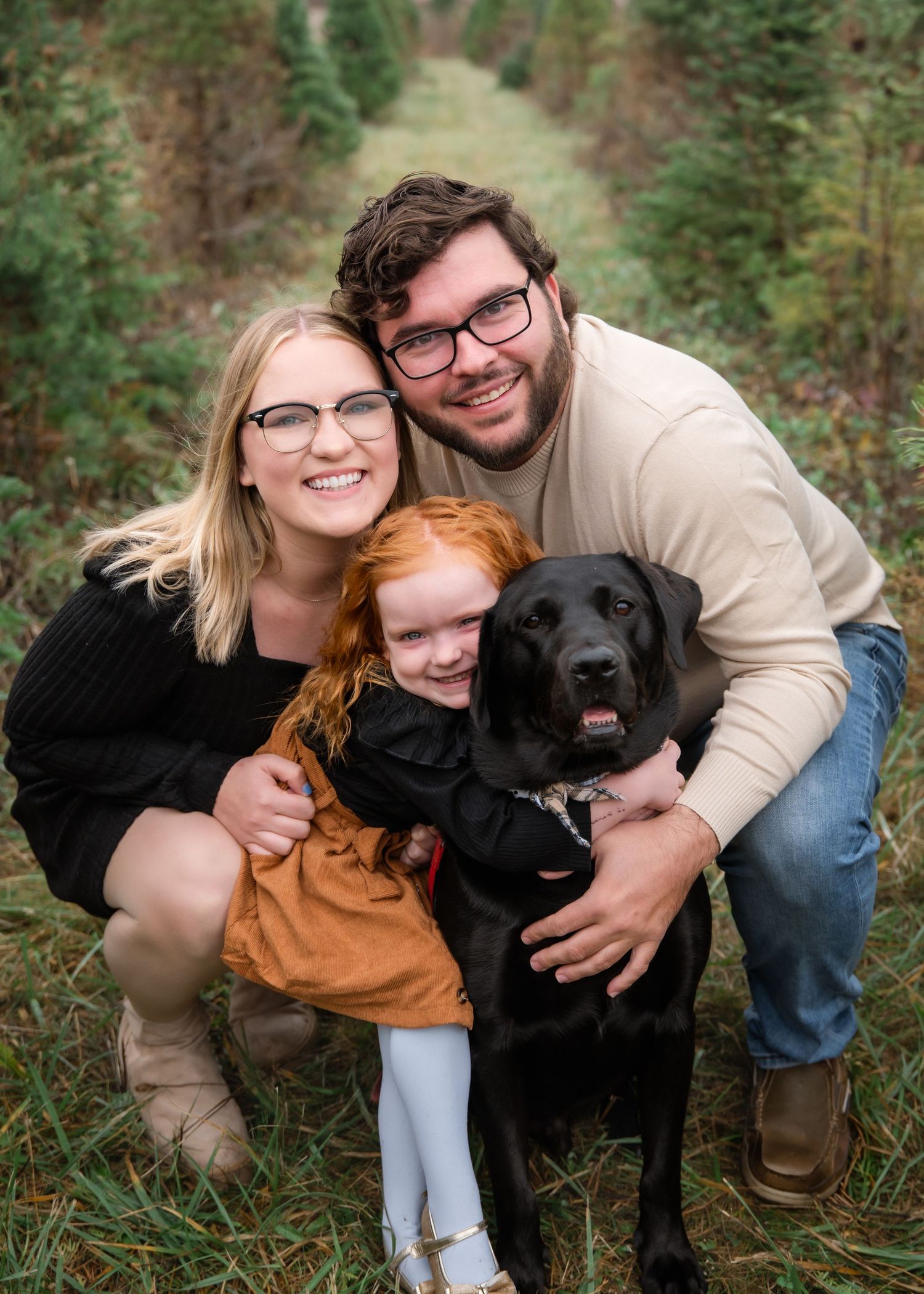 A family with their black dog poses together in a series of candid outdoor photos in nature.