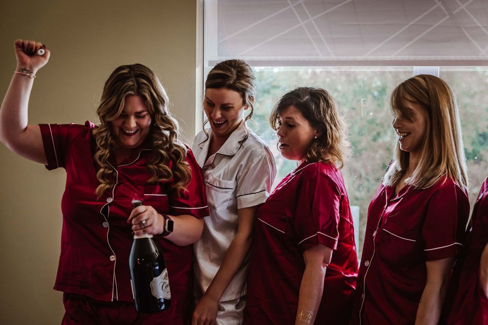 People in burgundy dresses gather together in a candid moment while getting ready for a formal occasion.
