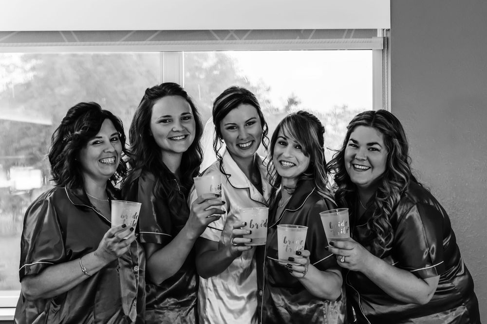 A group of five people sharing a celebratory moment with drinks while wearing matching robes in black and white photography.