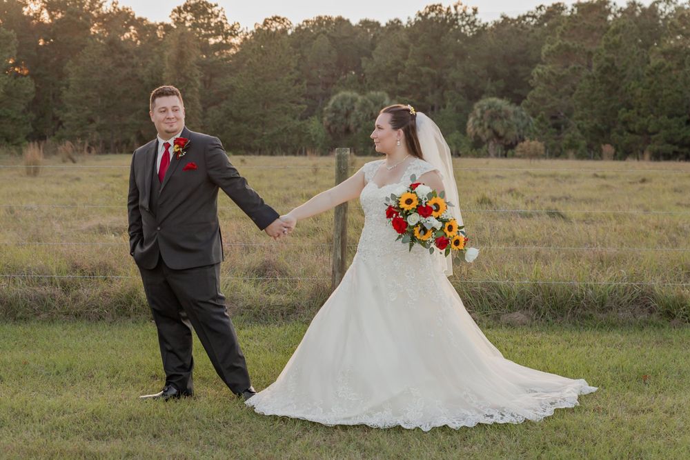 A couple poses for their wedding photos in a rustic field at sunset with vibrant fall colors in the background.