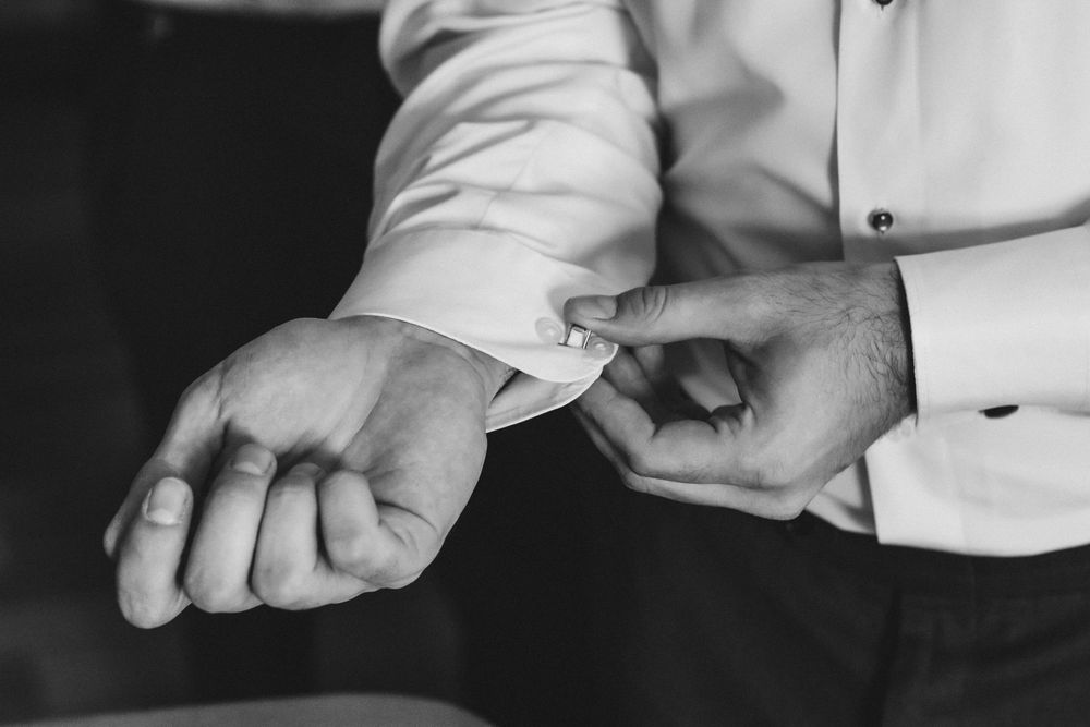 Black and white close-up photo of hands adjusting a dress shirt sleeve button.