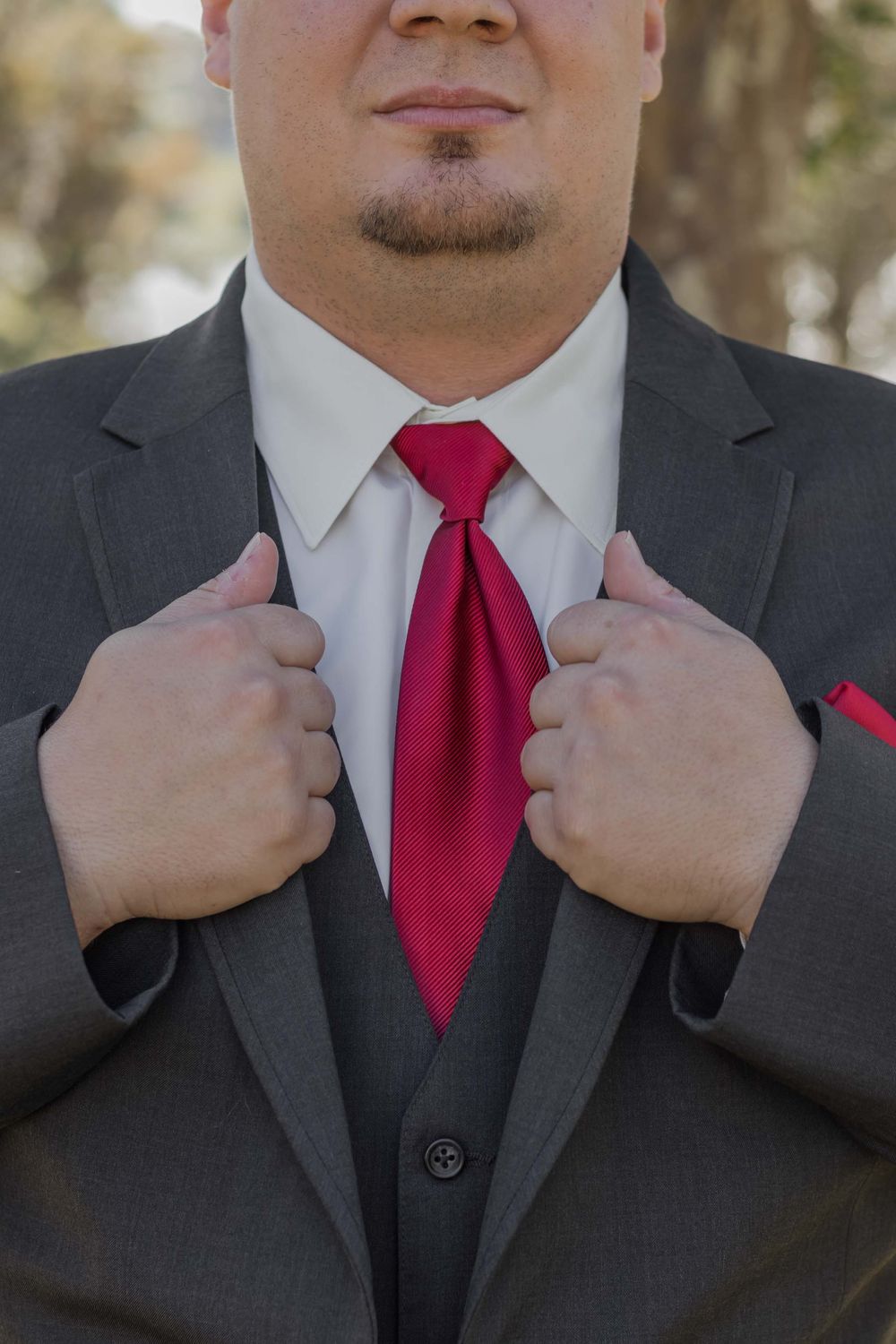 A close-up of a formal suit and tie combination showing a gray jacket, white shirt, and bright red necktie being adjusted.