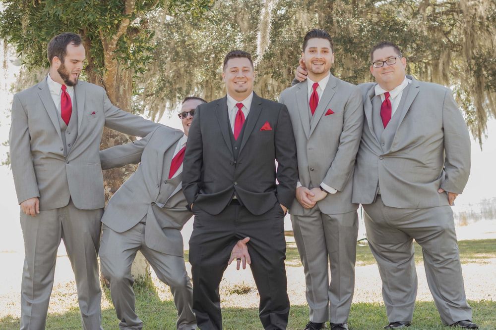 Wedding party members pose outdoors wearing grey suits with black and red accents.