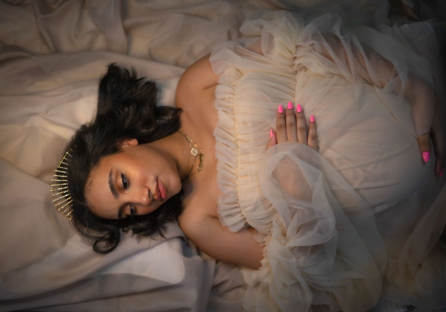 Elegant maternity portrait session with flowing white dress and dramatic lighting.