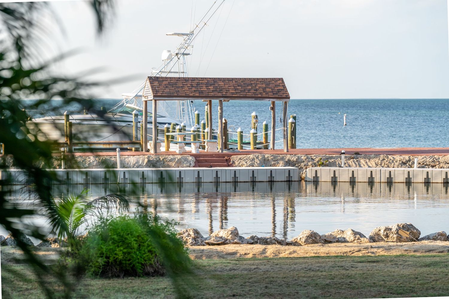 Oceanfront dock and pier extending into calm blue waters with tropical vegetation in foreground.