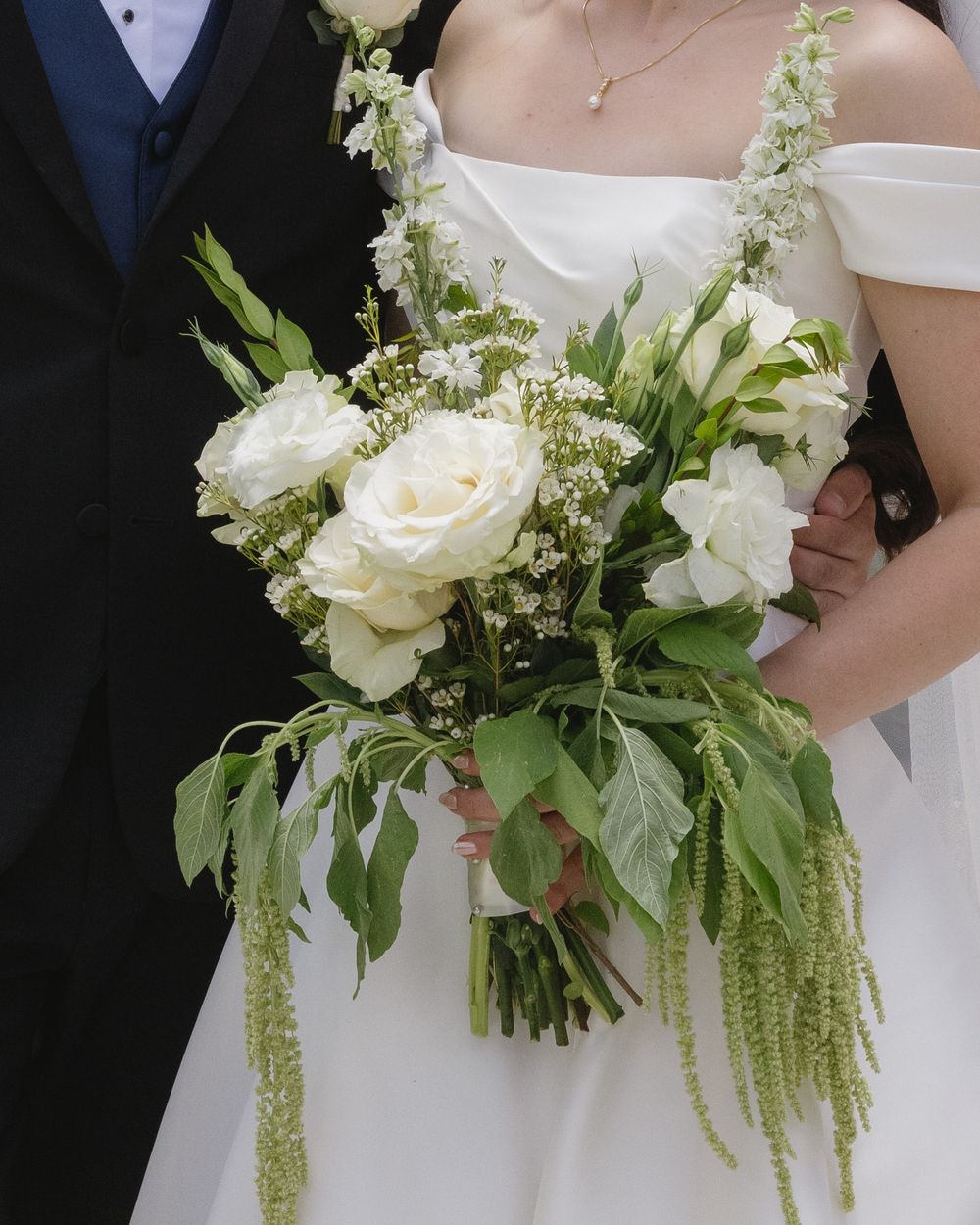 Wedding bouquet featuring white roses and trailing greenery with delicate cascading foliage details.