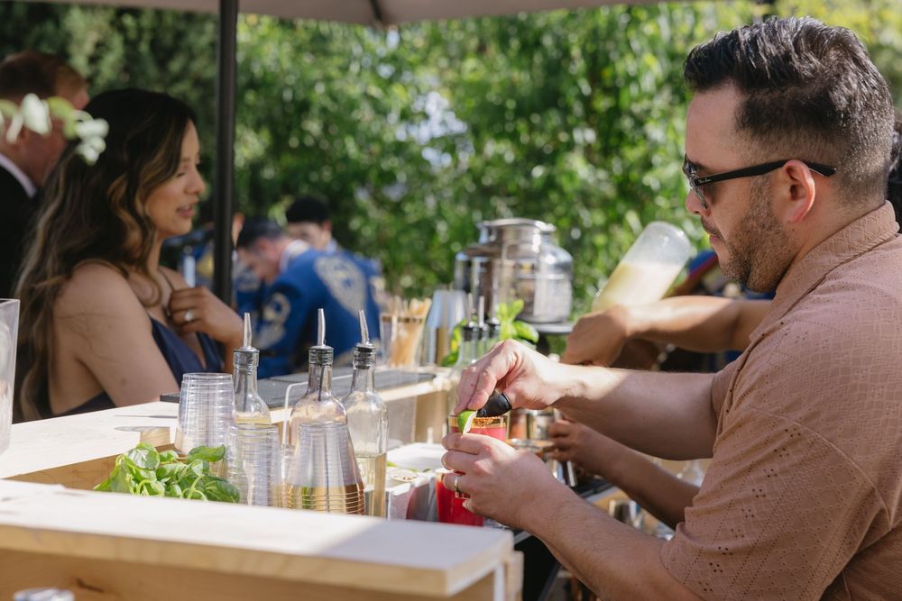 People enjoy drinks and conversation at an outdoor bar counter on a sunny day.