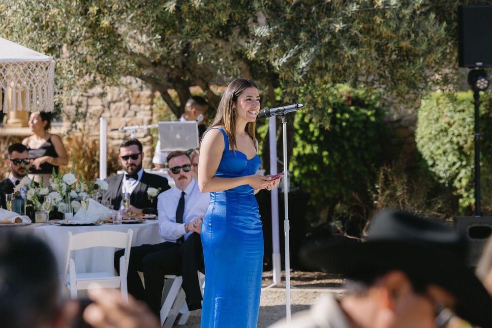 A group celebrates with toasts at an elegant outdoor wedding reception under a white tent in a garden setting.