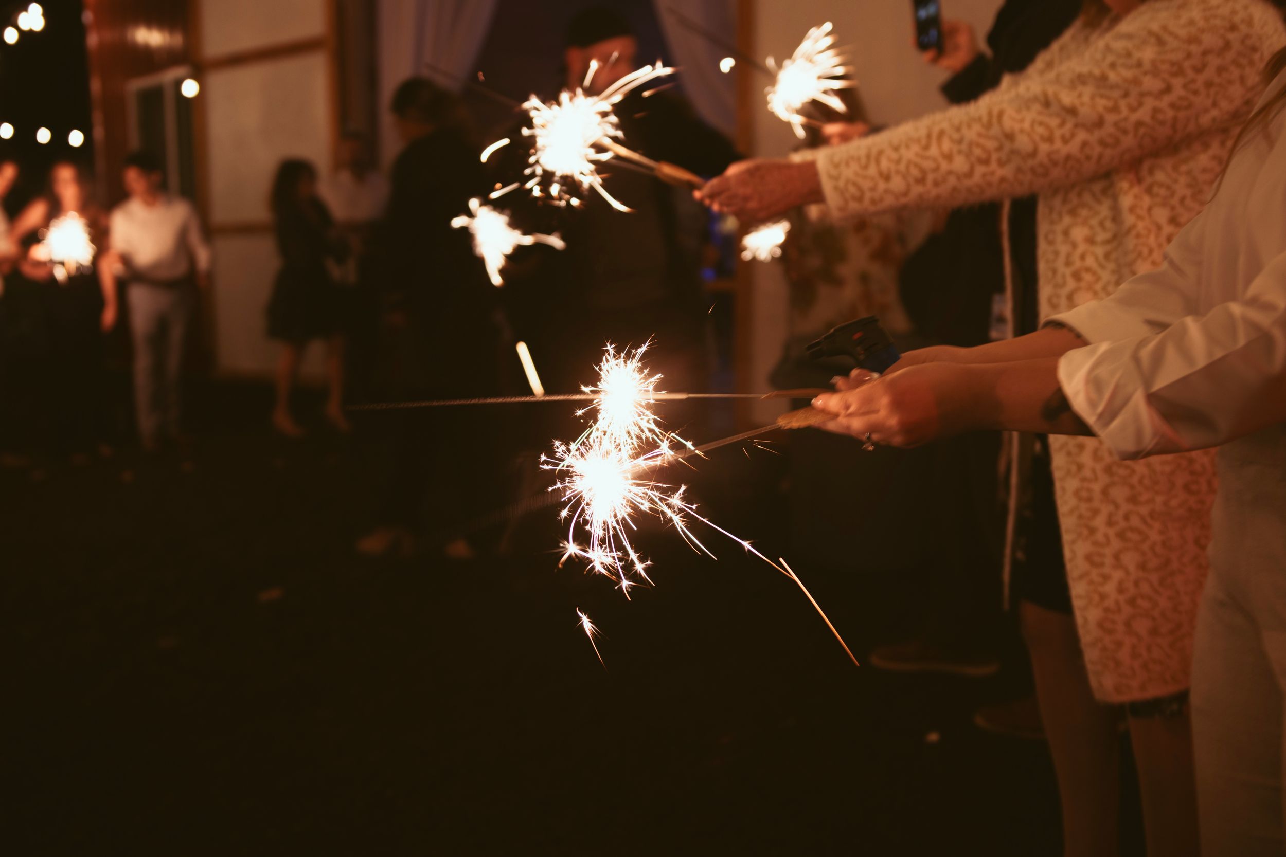 Wedding guests hold sparklers creating a magical nighttime celebration atmosphere.