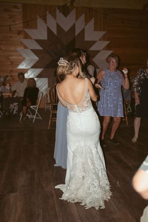 Wedding guests dance on a rustic wooden dance floor underneath string lights in a barn reception venue.