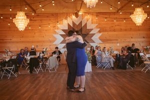 Wide view of rustic barn wedding reception space with chandeliers and wooden accent wall.