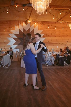 Couples dancing on hardwood floor under string lights in rustic barn venue.