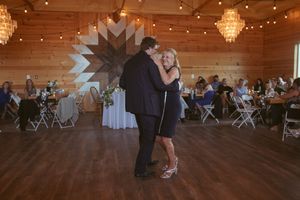 A couple dances in front of a geometric wall design at a rustic wedding reception venue.