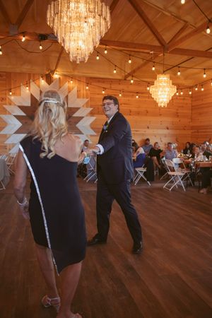 Couples dancing together under crystal chandeliers in a rustic wooden barn venue.