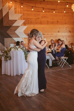 Two people share a dance moment on the wooden floor of a rustic wedding venue.