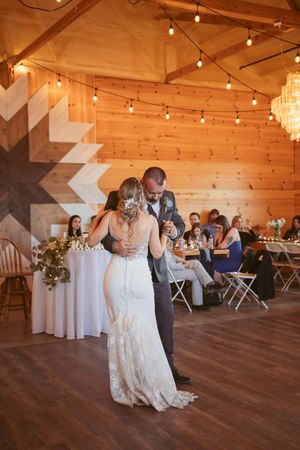 Couple dancing together during their first dance in a rustic wooden barn venue decorated with string lights.