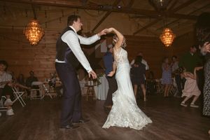 Guests watching as the newlyweds perform their first dance in a barn venue with string lights.