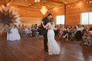 Wedding celebration inside a rustic wooden barn with crystal chandeliers and geometric wall art.
