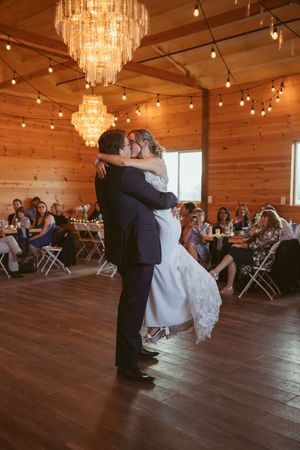 A romantic dance moment in a rustic venue with chandeliers and string lights.