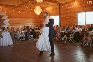 Dancers perform during a reception in a rustic wooden venue decorated with string lights and crystal chandeliers.
